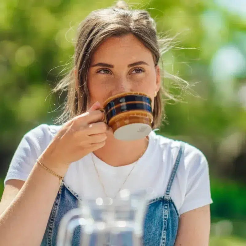 En kvinna sitter utomhus i solen och tar en lugn kaffepaus. Bilden förmedlar en trygg vardag och illustrerar Falkenberg Energis information om hur elpriser fungerar och jämförs.