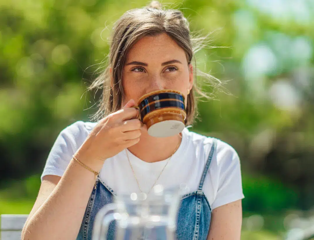En kvinna sitter utomhus i solen och tar en lugn kaffepaus. Bilden förmedlar en trygg vardag och illustrerar Falkenberg Energis information om hur elpriser fungerar och jämförs.