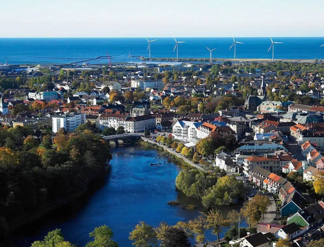 En vacker flygbild över Falkenberg som visar staden, ån Ätran och vindkraftverk ute vid kusten. Bilden förmedlar den lokala tryggheten hos Falkenberg Energi, som smidigt tar hand om hela processen efter att du har tecknat ditt elavtal.